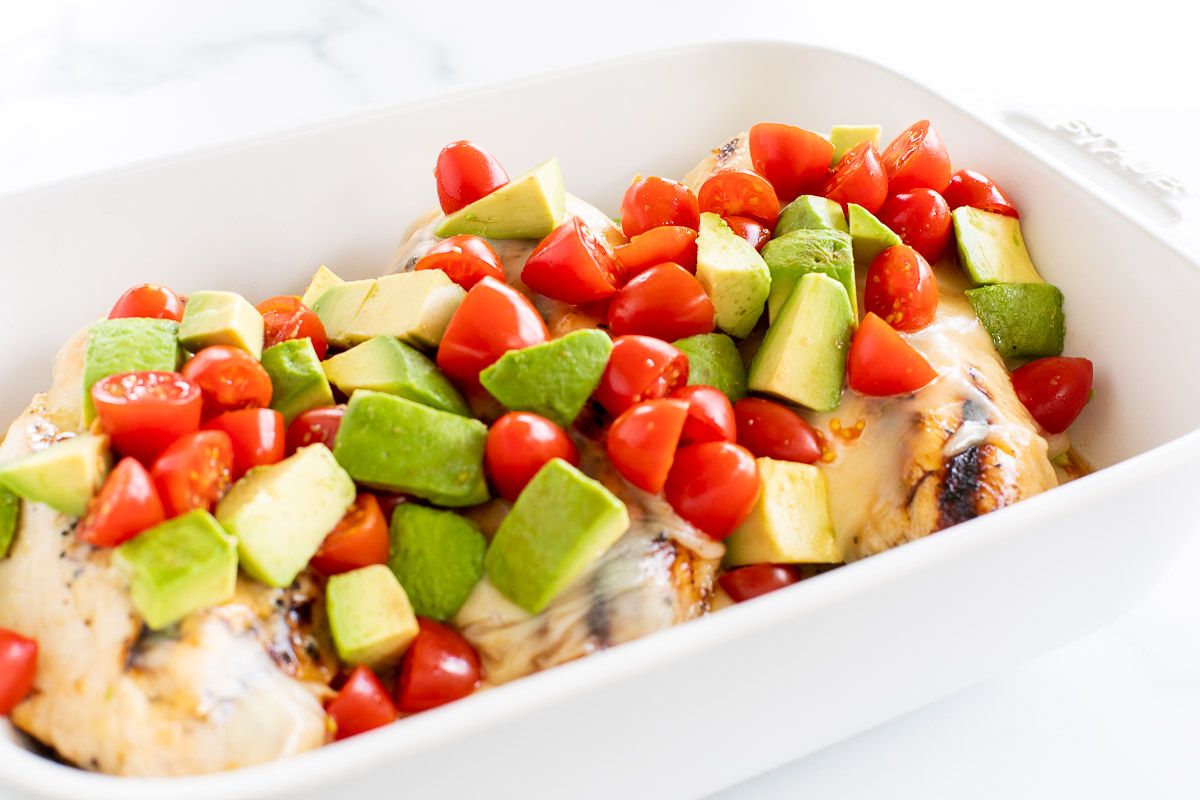 A white baking dish full of california chicken topped with diced tomatoes and avocados.