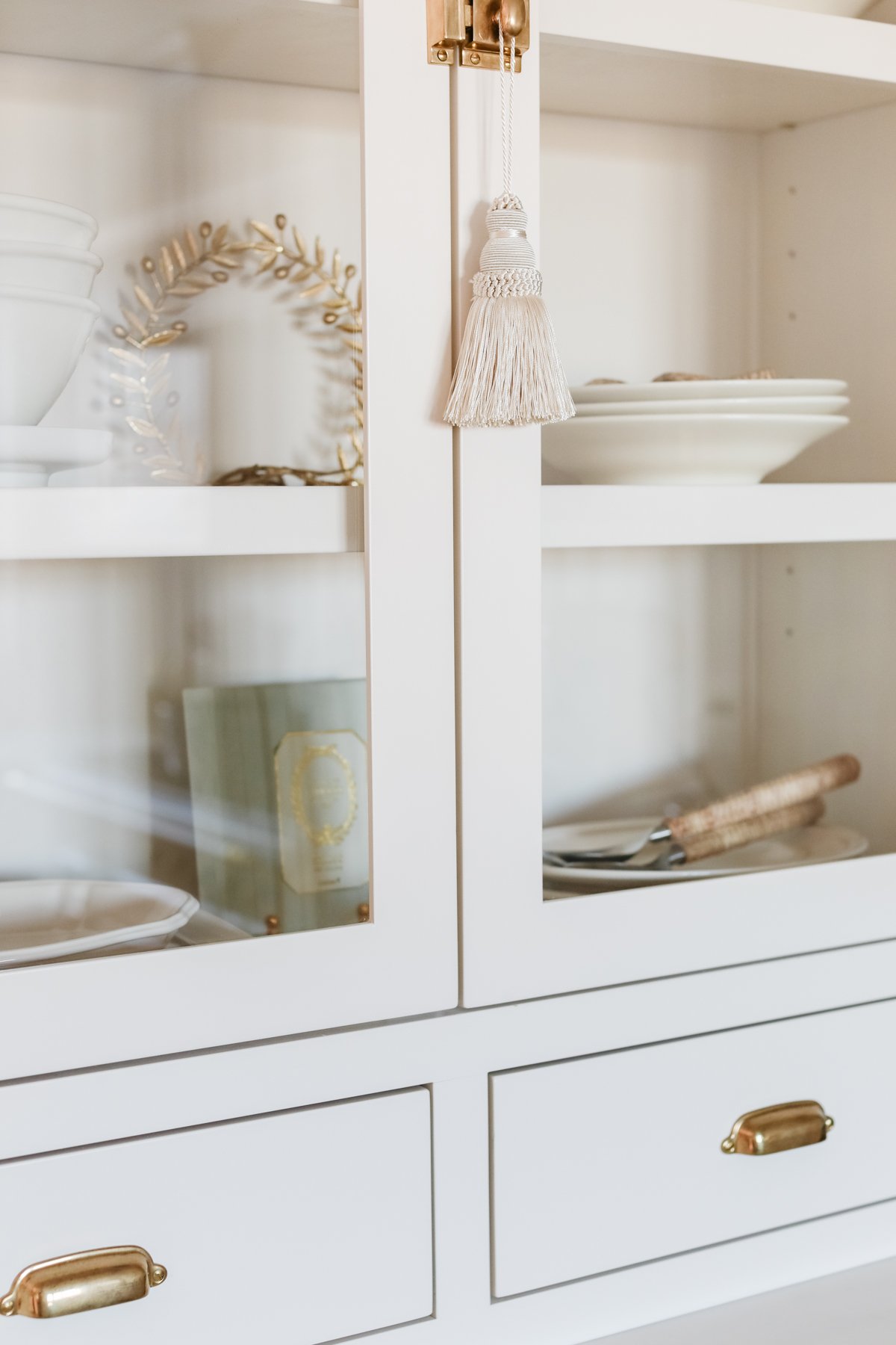 A high end white china cabinet with a gold tassel on the door.