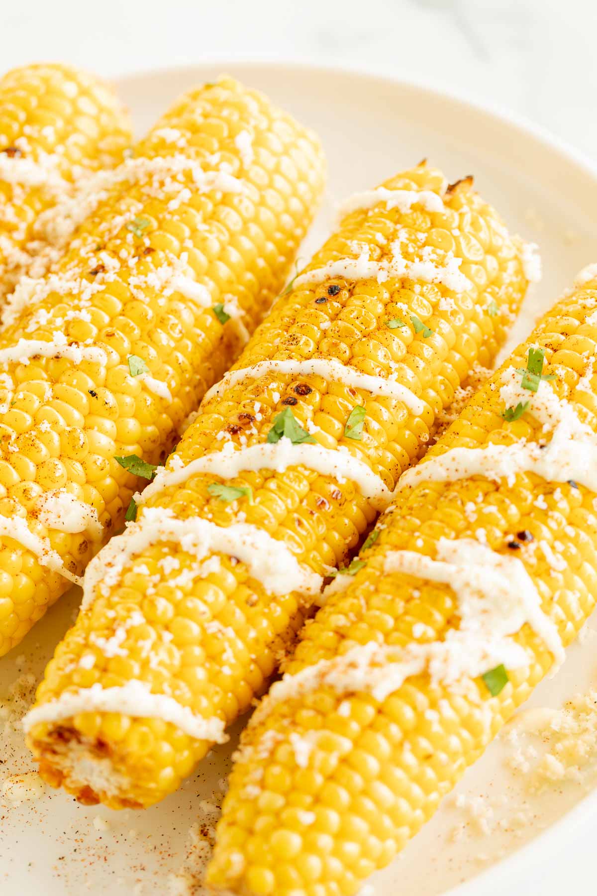 Elote (Mexican corn on the cob) drizzled with crema on a white plate.