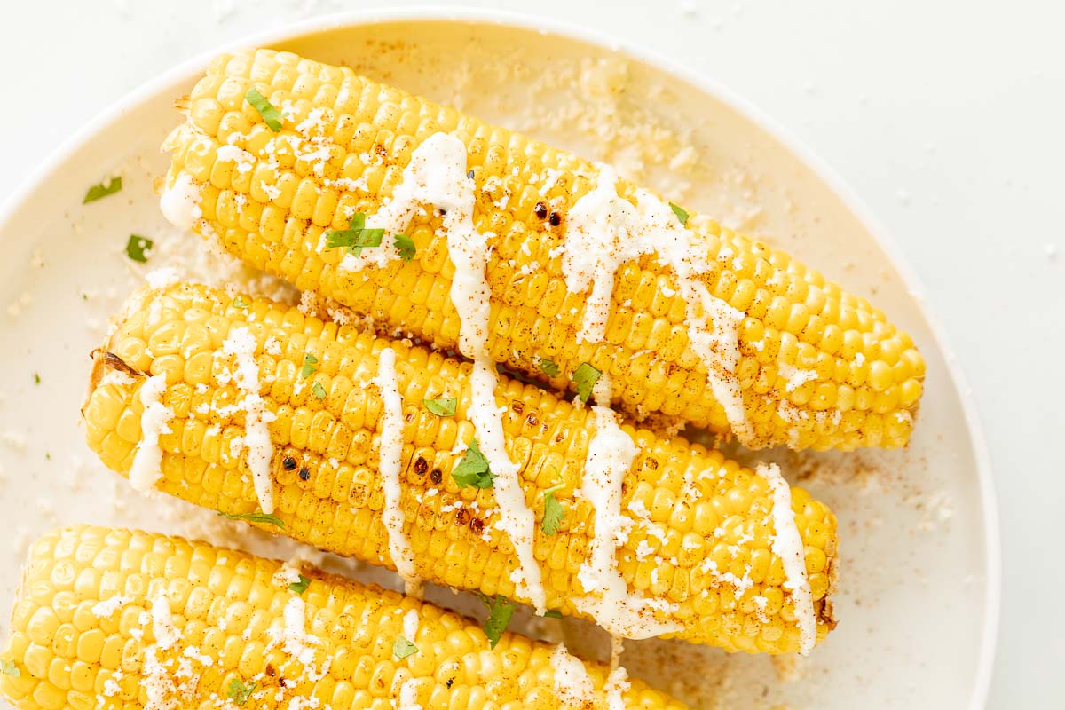 Elote (Mexican corn on the cob) drizzled with crema on a white plate.