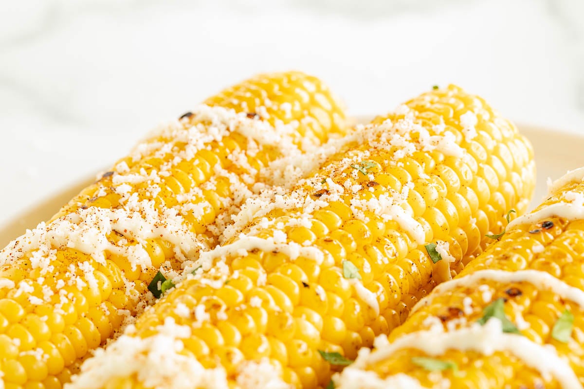 Elote (Mexican corn on the cob) drizzled with crema on a white plate.