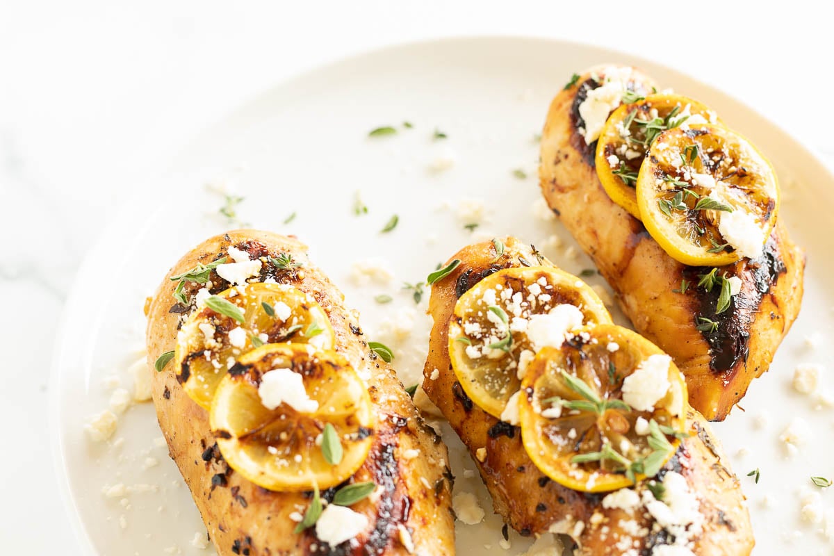 Greek chicken on a white plate, grilled lemon slices on top.