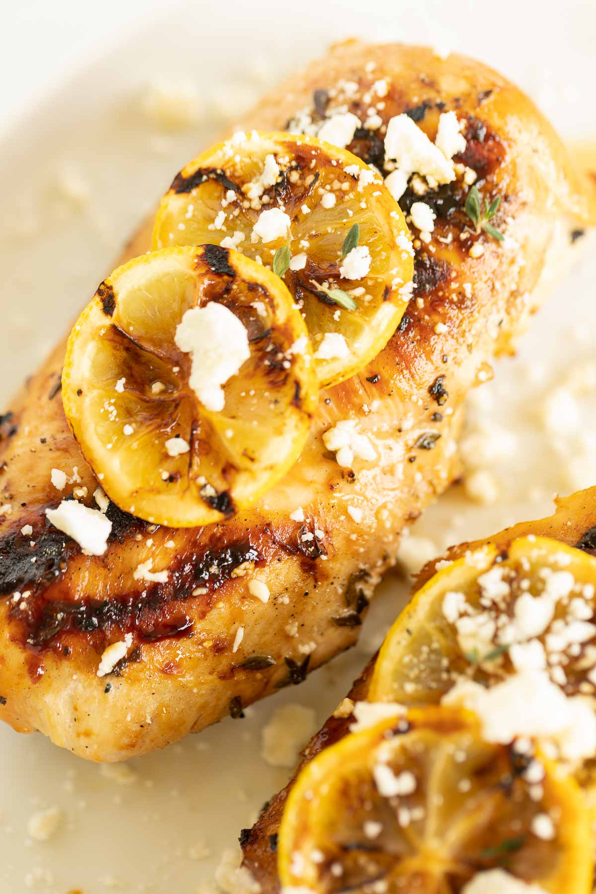 Greek chicken on a white surface, grilled lemon to the side.