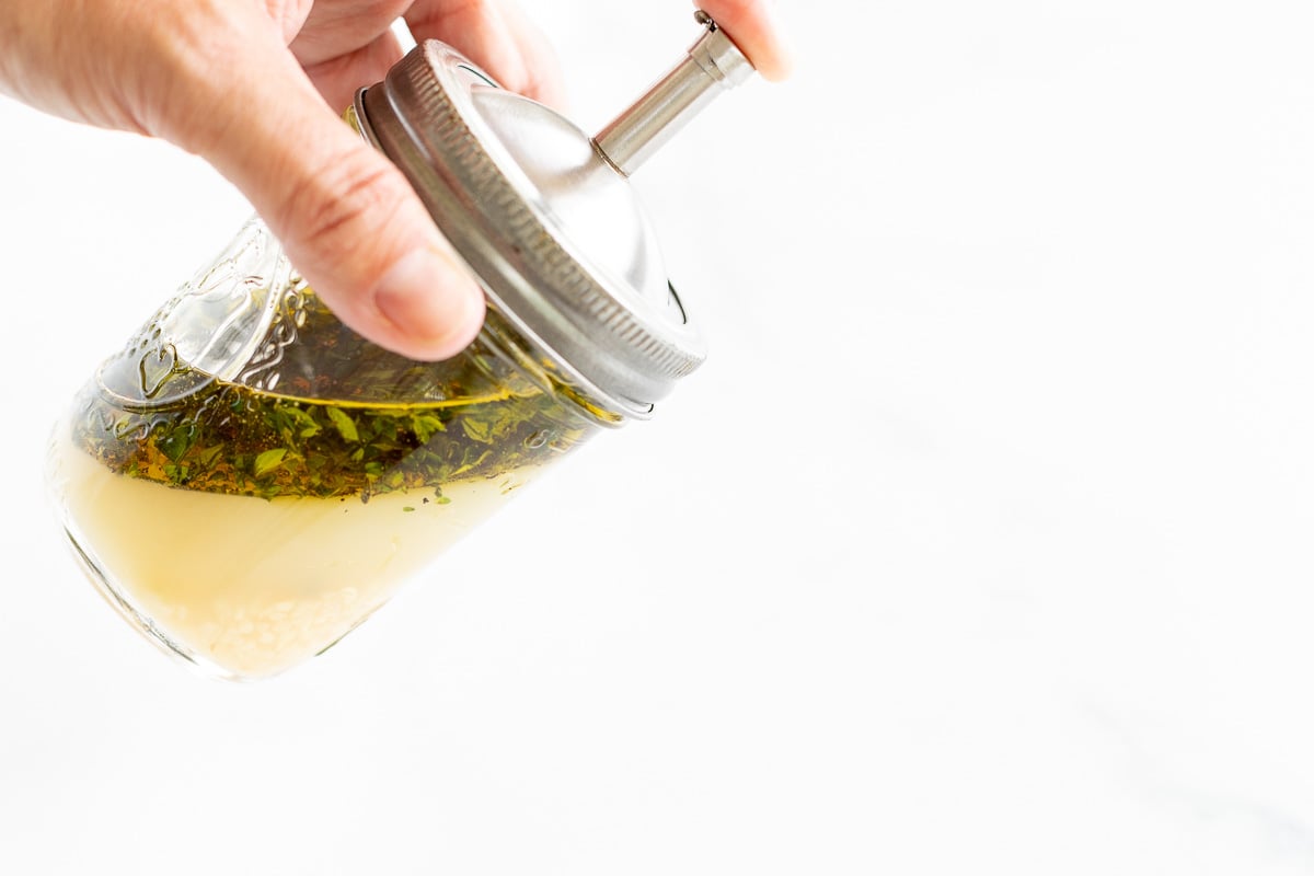 A hand holding a glass jar full of marinade.