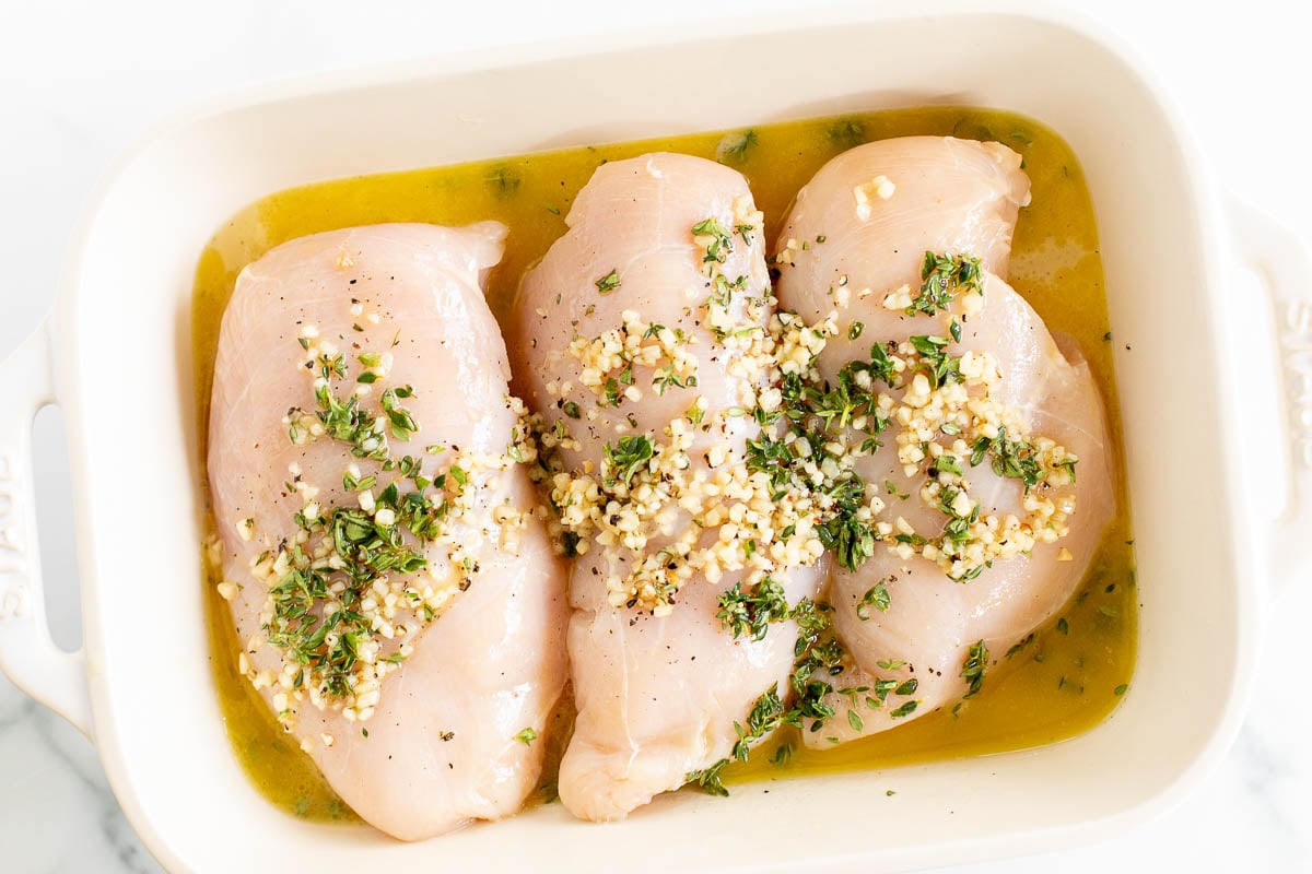 Marinated Greek chicken breasts in a white baking dish.