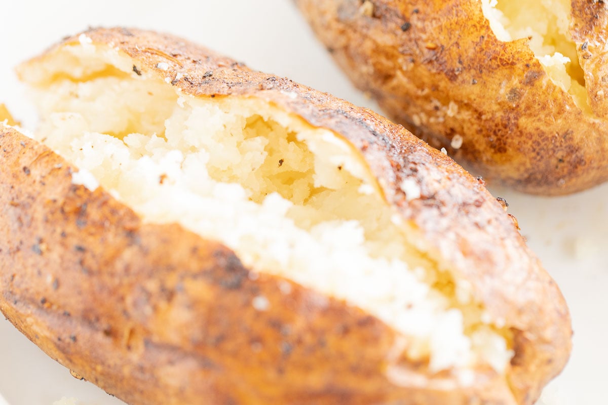 grilled baked potatoes sliced open and placed on a white plate.