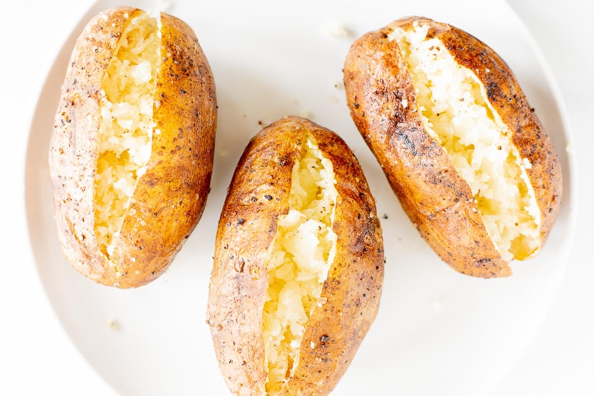 grilled baked potatoes sliced open and placed on a white plate.