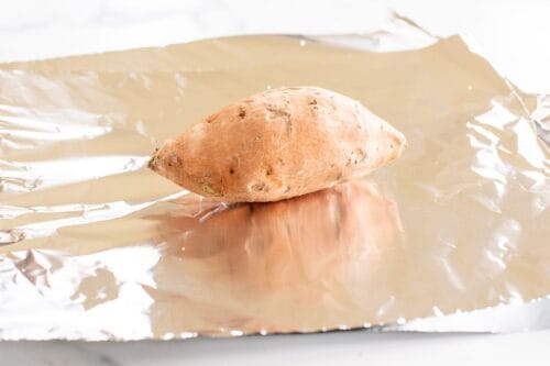 A sweet potato resting on a piece of aluminum foil.