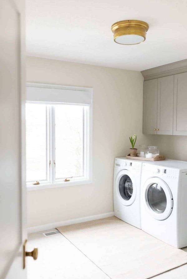 A laundry room with white washer and dryer, gold light fixture and white walls and white baseboards