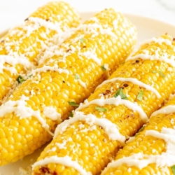 Elote (Mexican corn on the cob) drizzled with crema on a white plate.