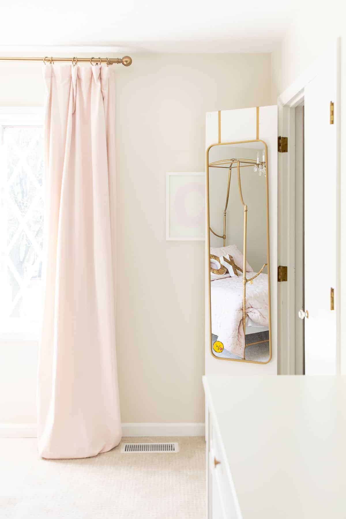 A girl's bedroom with pink curtains, light carpet and white painted baseboards.