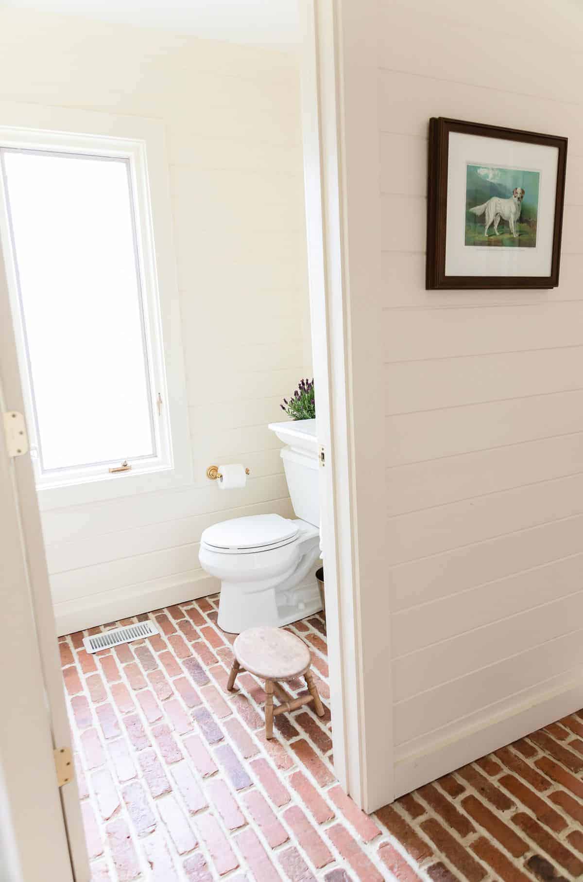 A white bathroom with white shiplap, white painted baseboards and brick floors, 