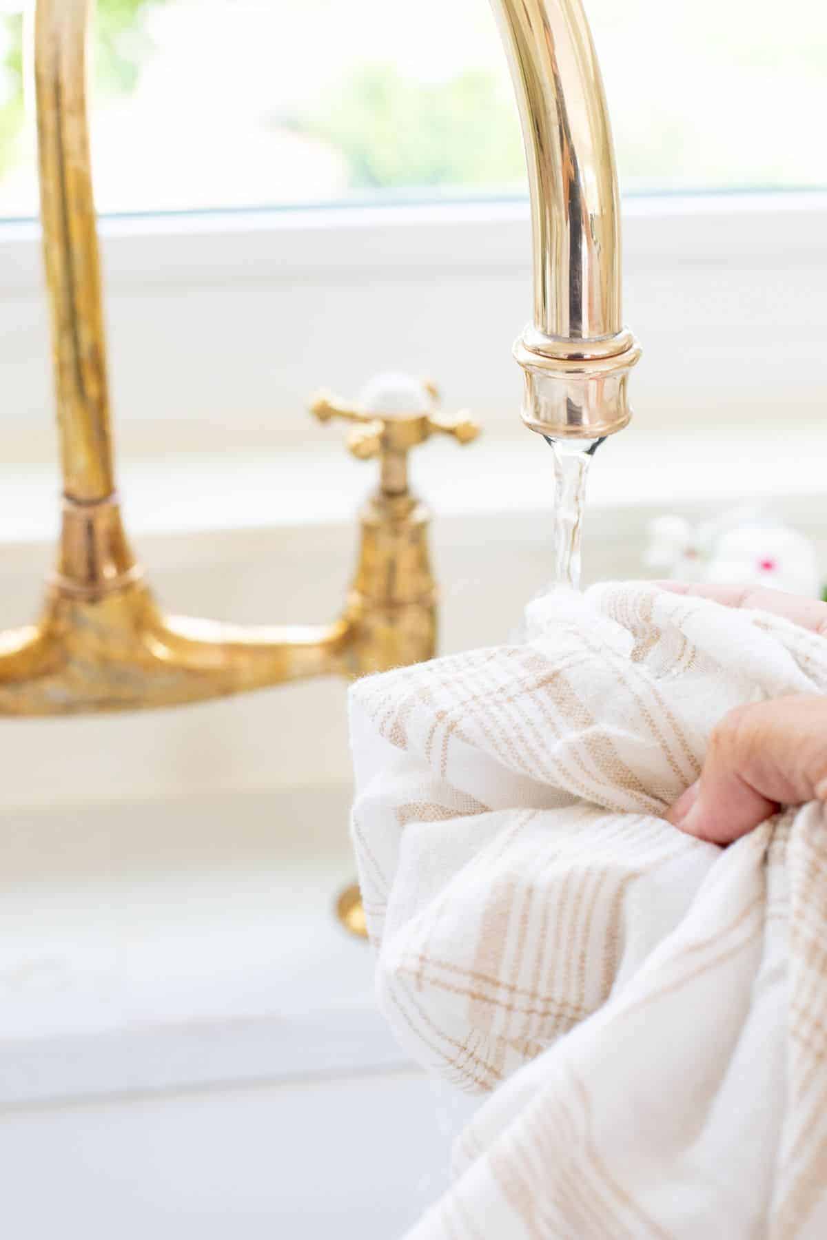 A tarnished brass faucet with water running out onto a scrubbing cloth.