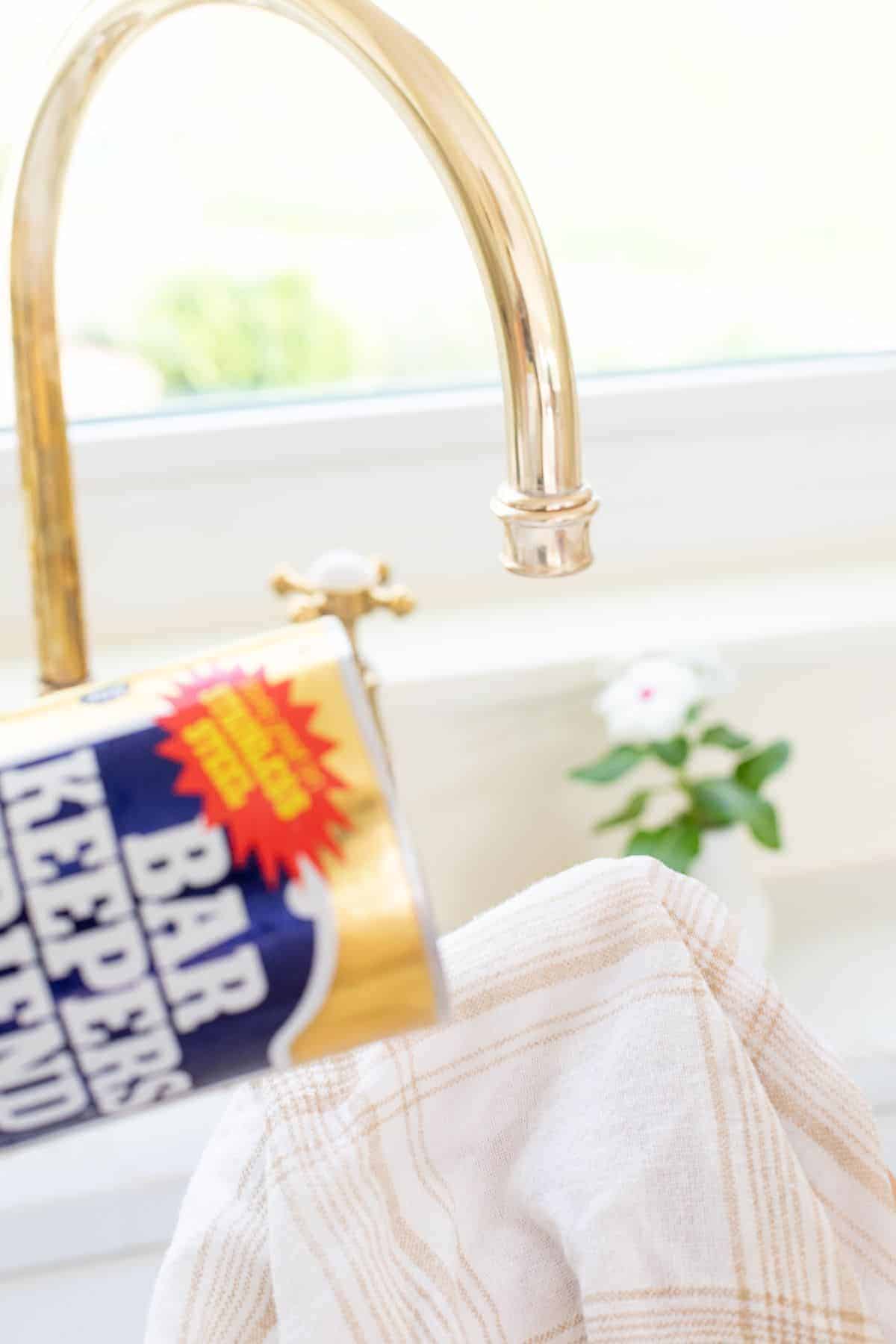 A tarnished brass faucet being scrubbed with a soft cloth and the best brass polish.