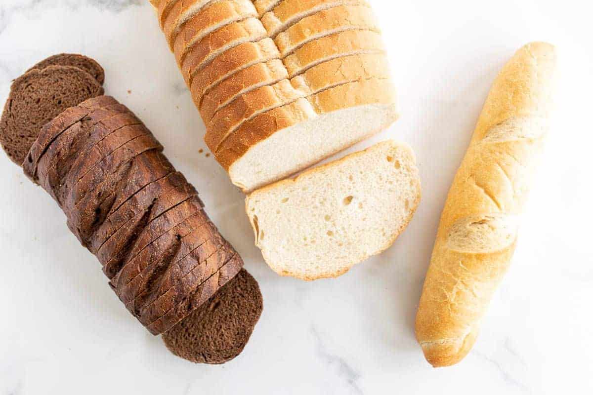 Three different loaves of bread on a marble surface, in a post about the best bread for grilled cheese.