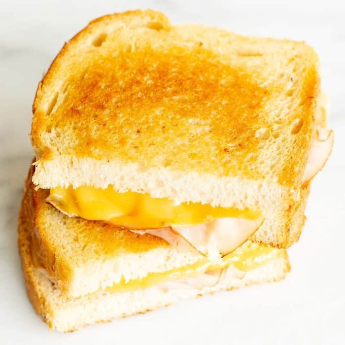 A grilled cheese sandwich with ham, sliced in half and stacked on a marble surface.