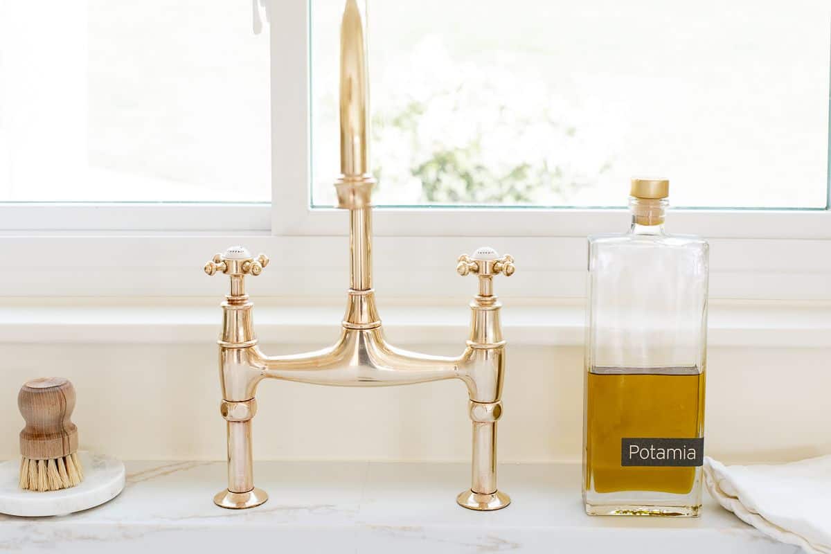 A brass bridge faucet that is shiny from brass polish, bottle of olive oil to the side.