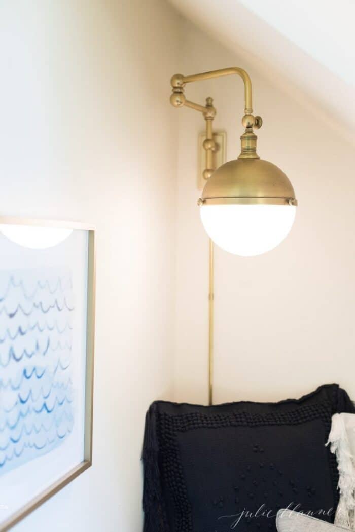 A nook under the stairs of a home with pillows, a wall sconce and art.