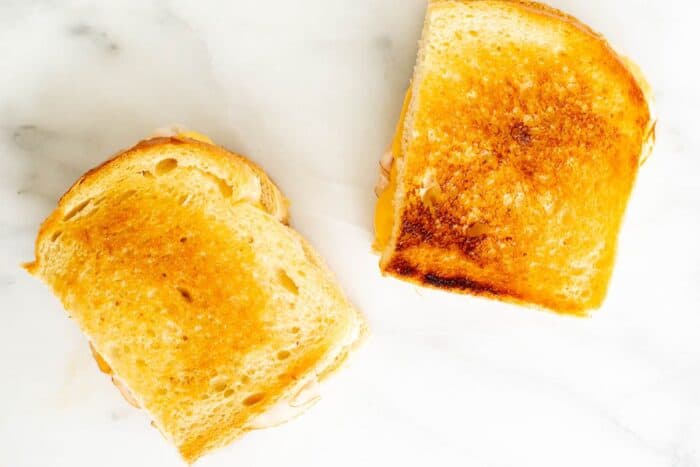 A sliced grilled ham and cheese on a white marble surface.