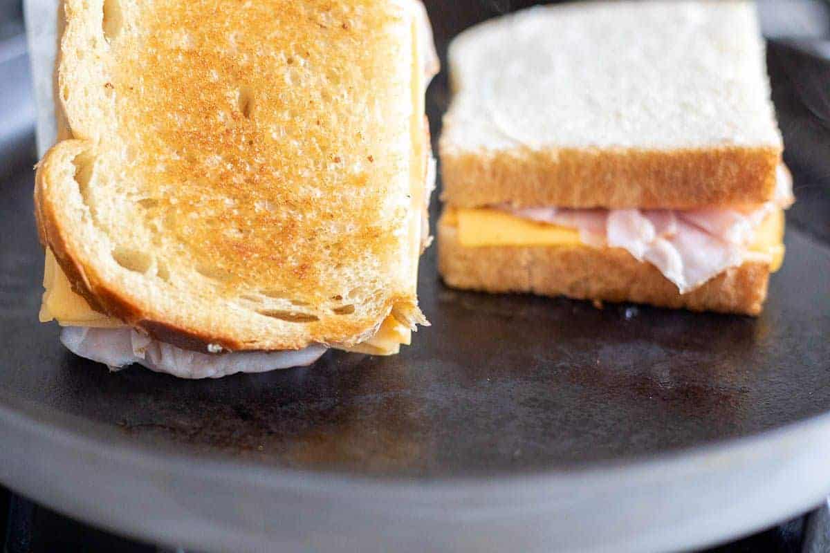 Two grilled ham and cheese sandwiches on a black cast iron pan.
