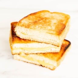 A stack of sliced grilled cheese with mayonnaise on a white marble surface.