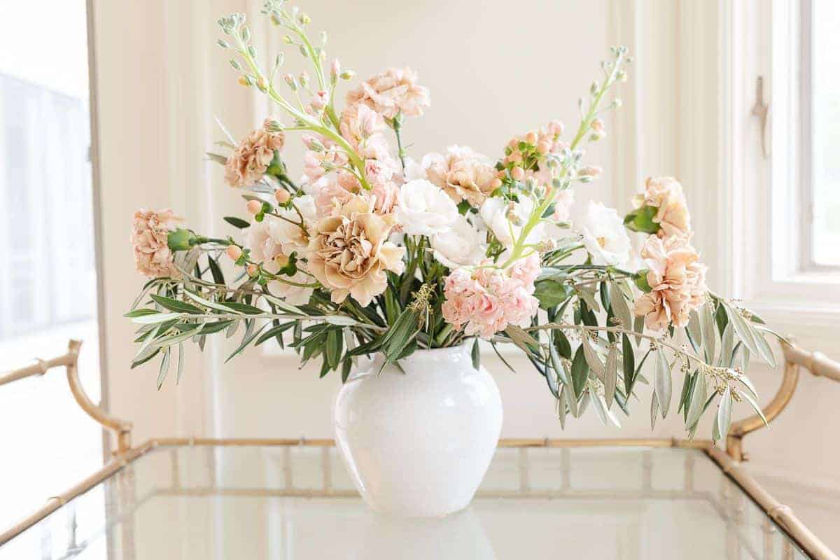 Antique Pink carnation arrangement on a brass bar cart in a cream room.