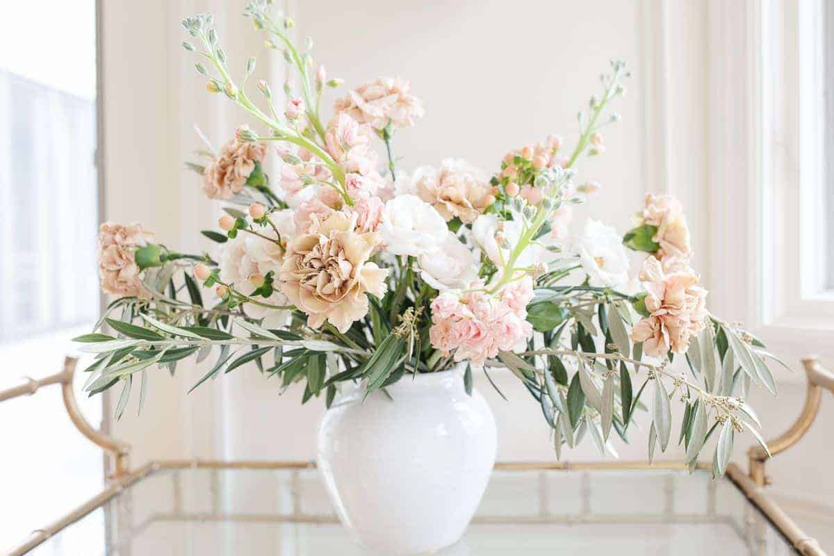 Antique carnations, stock and greenery in a white vase against a white background.