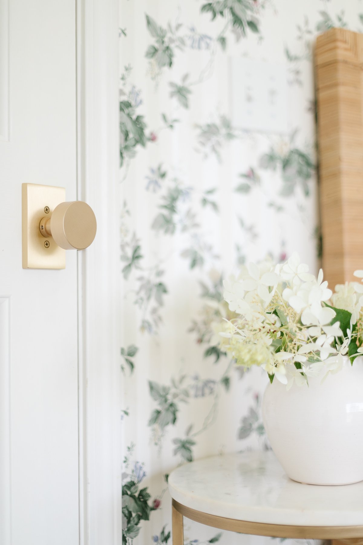 A bedroom with floral wallpaper with modern brass door knobs on the doors.