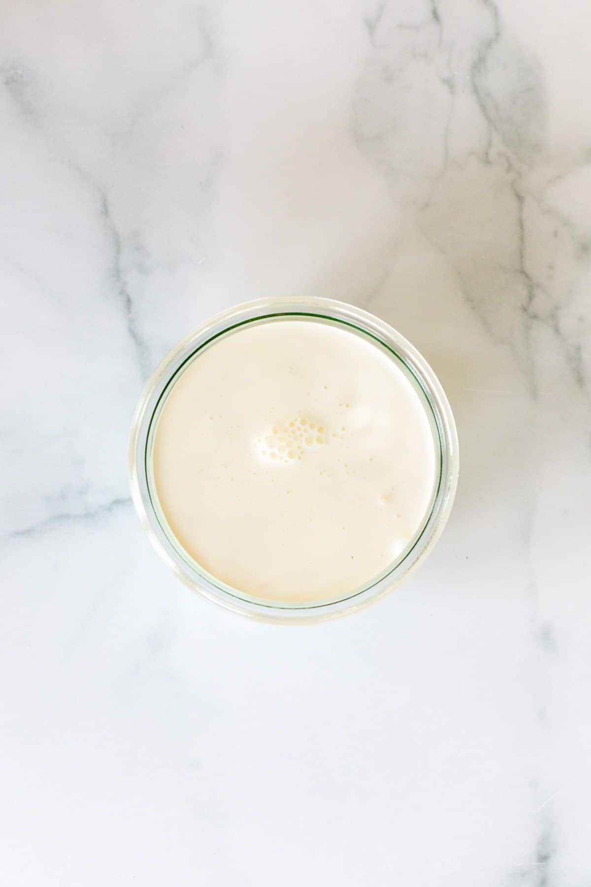 Heavy whipping cream in a small clear glass jar on a marble surface.