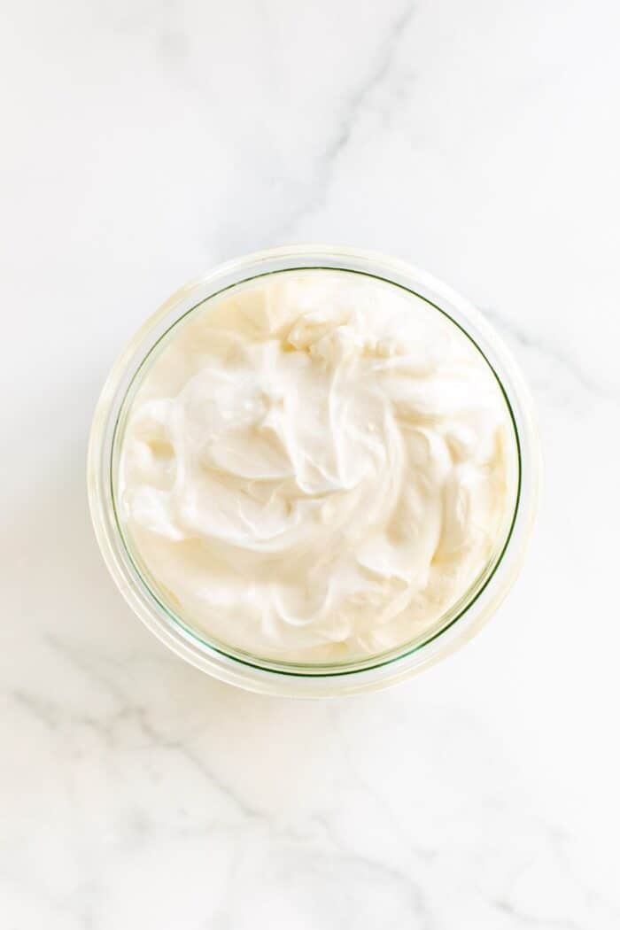 A small glass jar of creme fraiche substitute on a white marble surface.