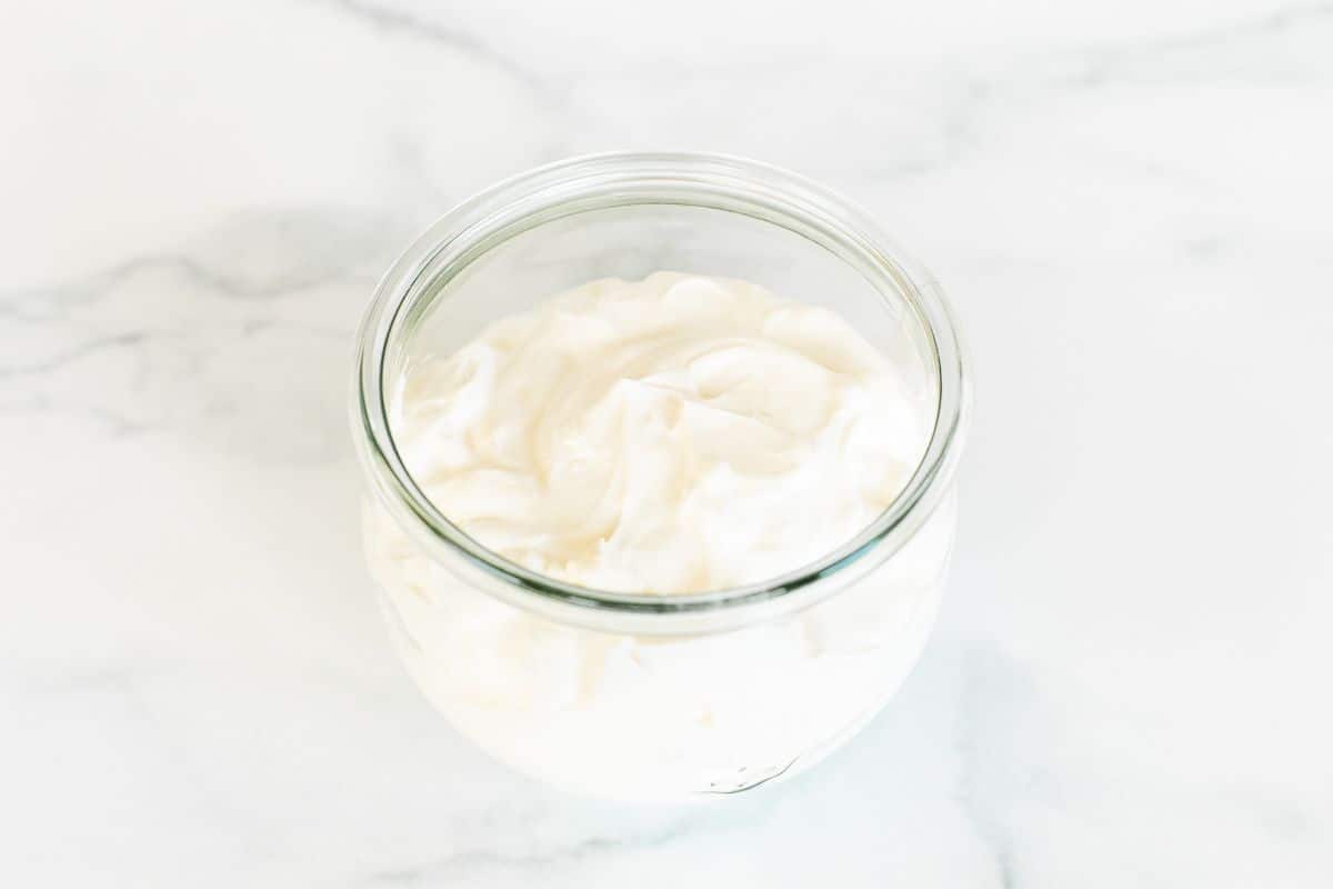 A small glass jar of creme fraiche alternative on a white marble surface.