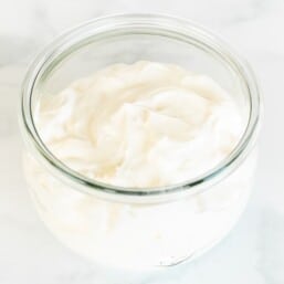 A small glass jar of creme fraiche substitute on a white marble surface.