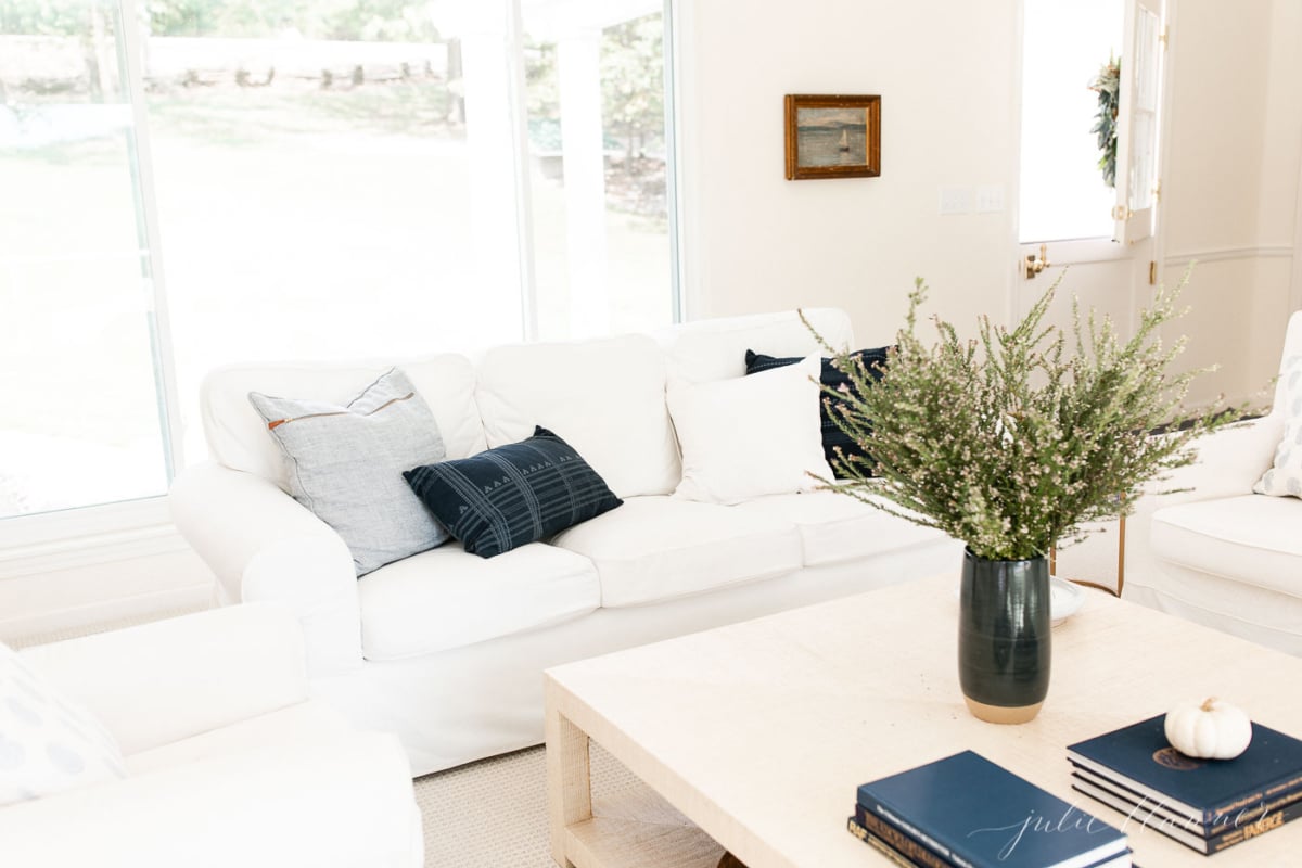 A minimalist living room adorned with white couches and a vase of flowers, featuring subtle fall decor elements.