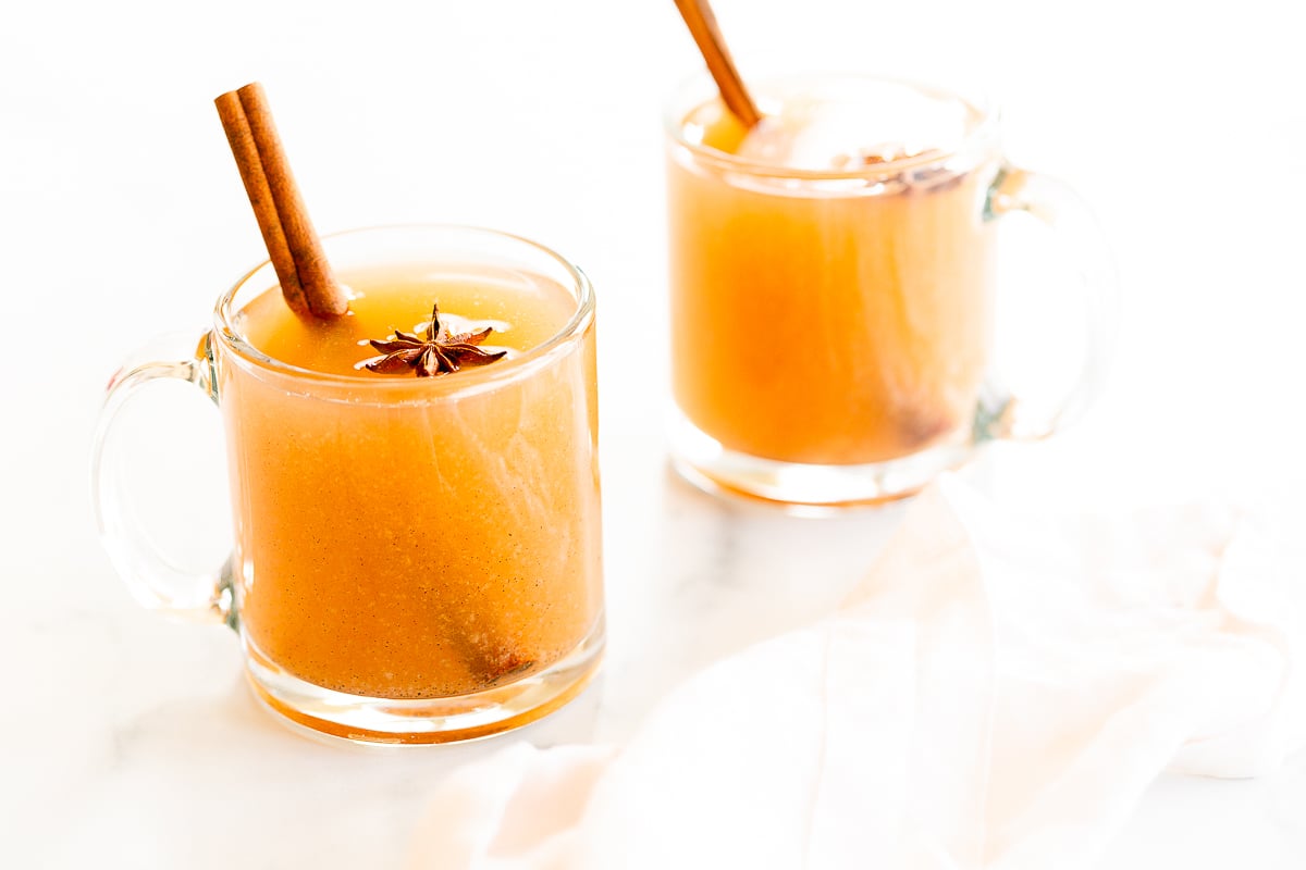 two clear glass mugs of pear cider on a white surface
