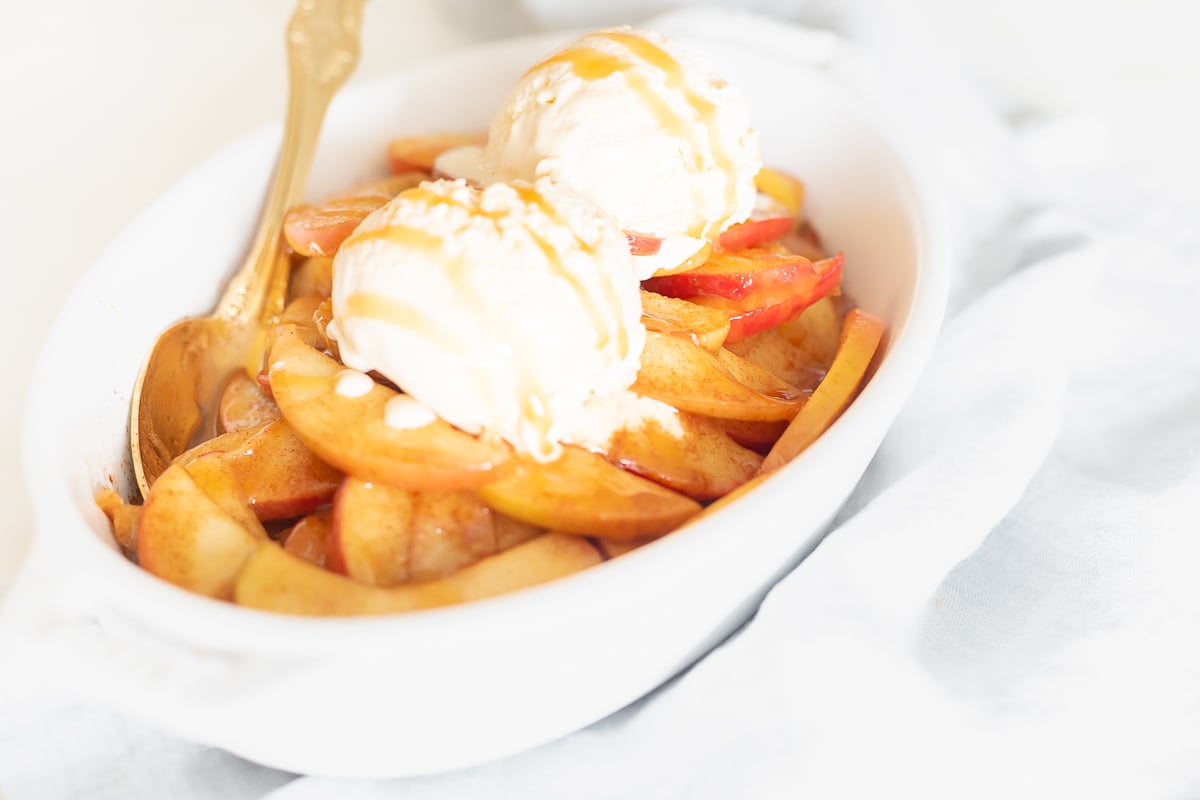 A bowl filled with baked apple slices and ice cream.