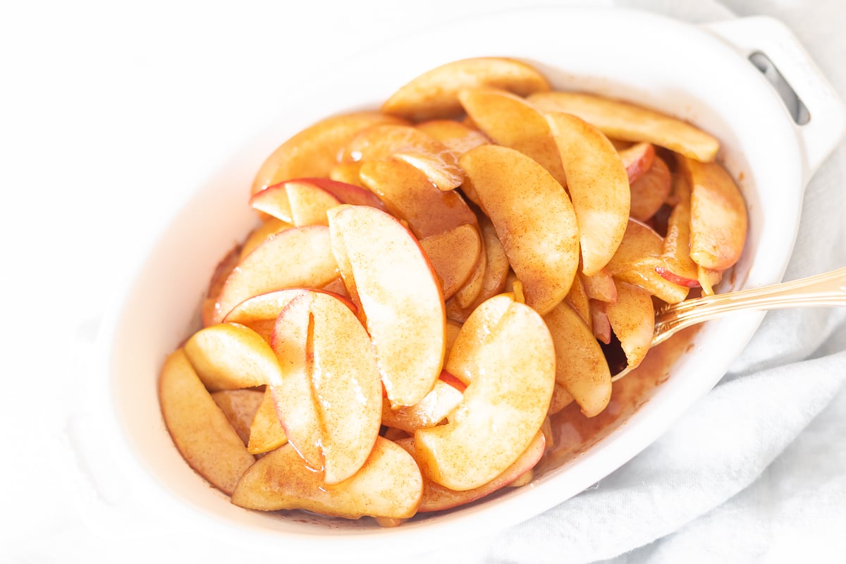 Baked apple slices arranged in a white bowl with a spoon.