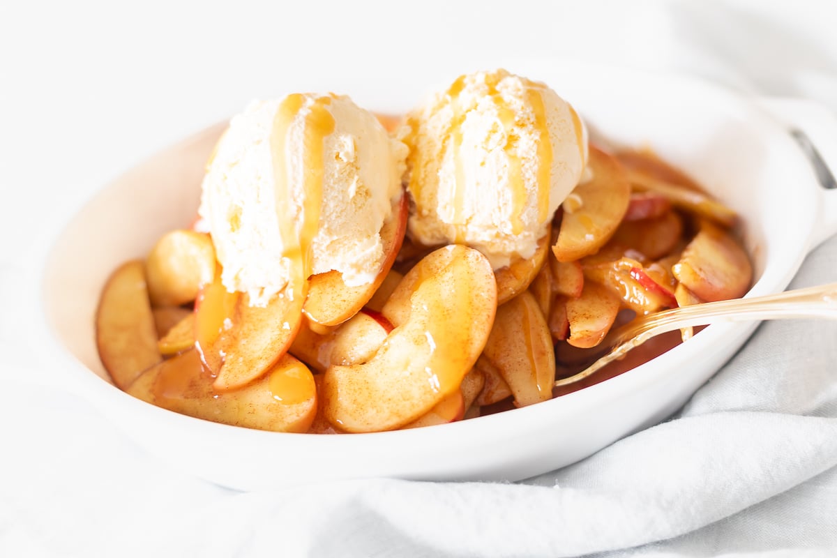 A white bowl filled with baked apple slices and ice cream.