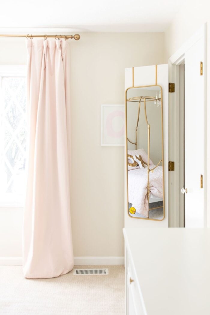 A girl's bedroom with pink blackout curtains and a mirror hanging on a closet door.