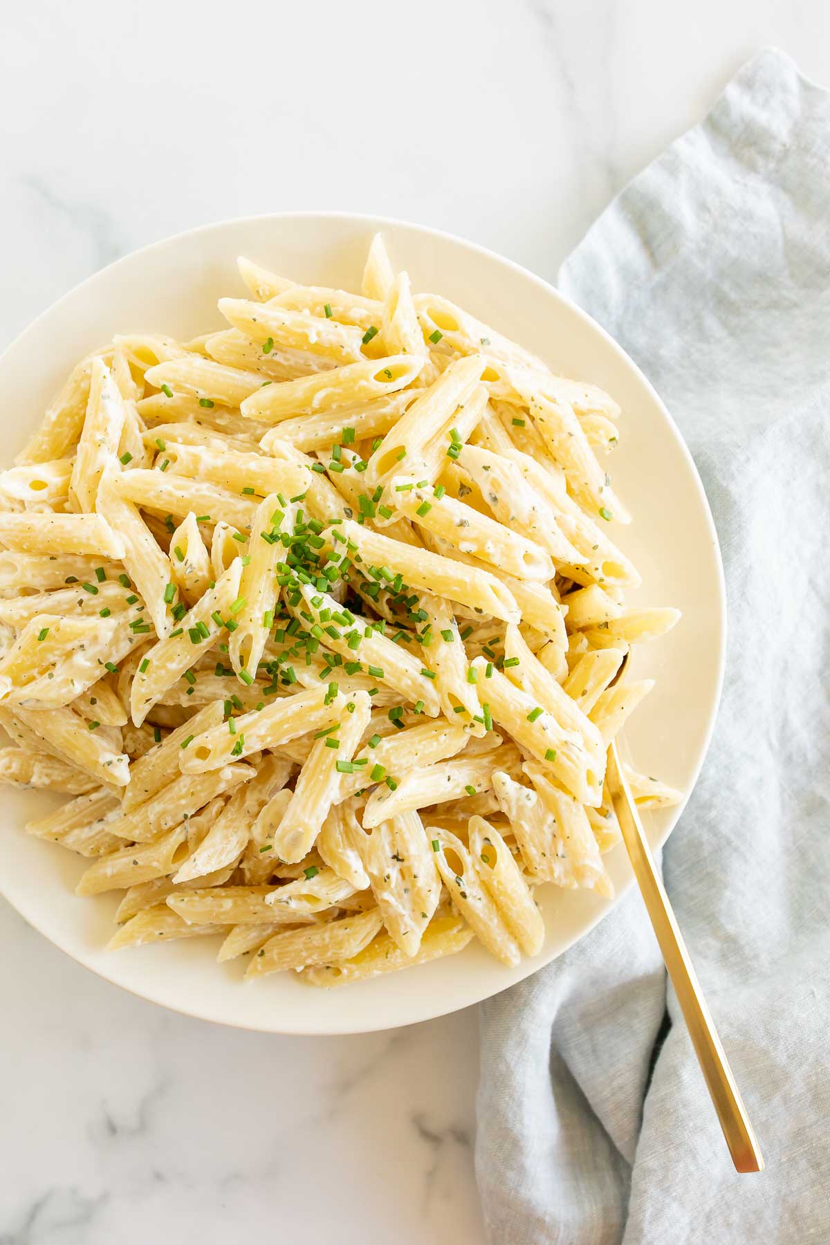 A white serving bowl full of Boursin pasta topped with chives.