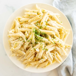 A white serving bowl full of Boursin pasta topped with chives.