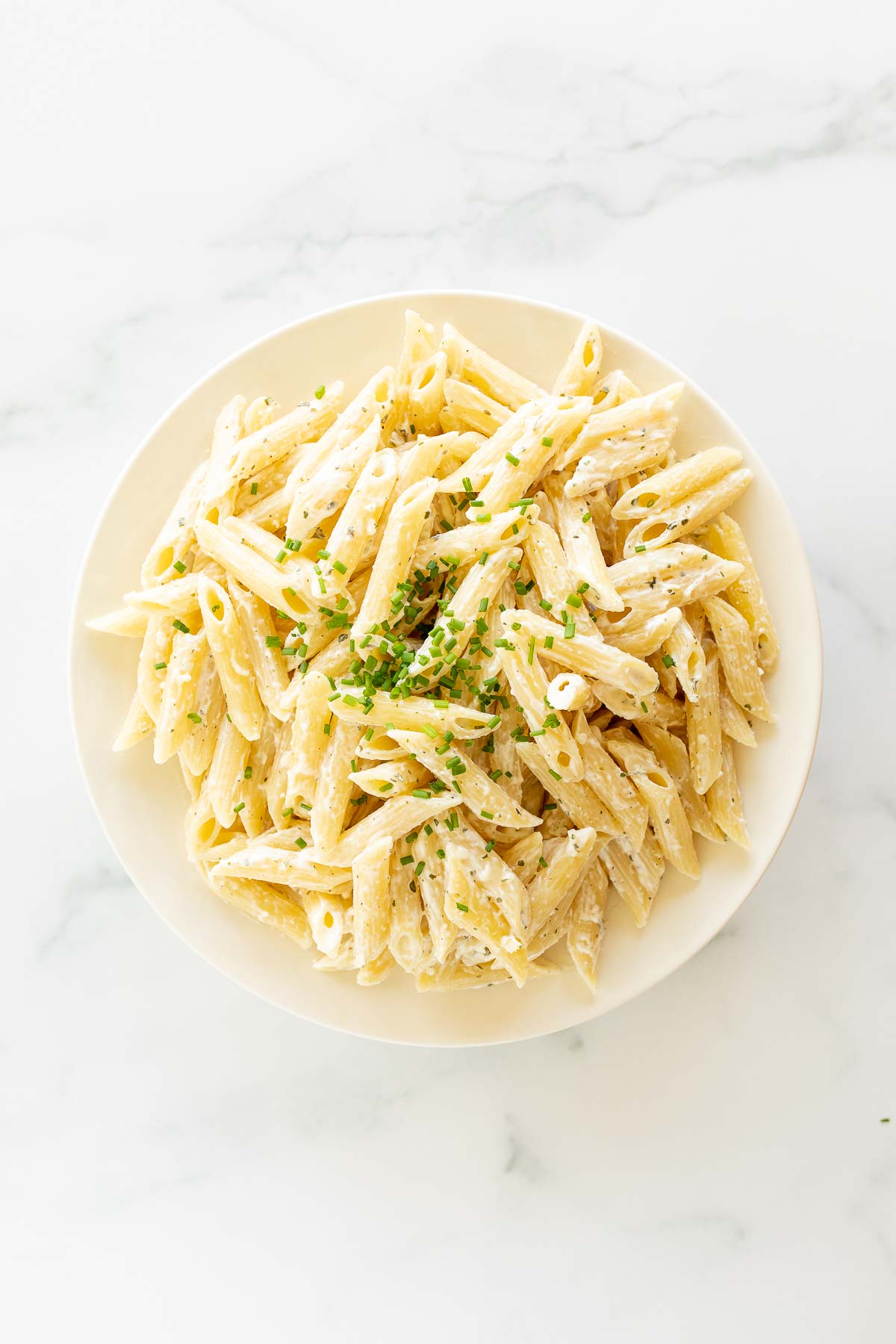 A white serving bowl full of Boursin pasta topped with chives.