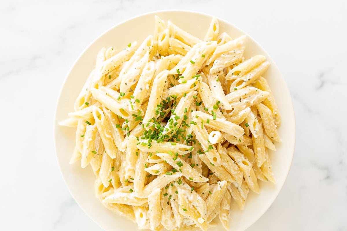 A white serving bowl full of Boursin pasta topped with chives.