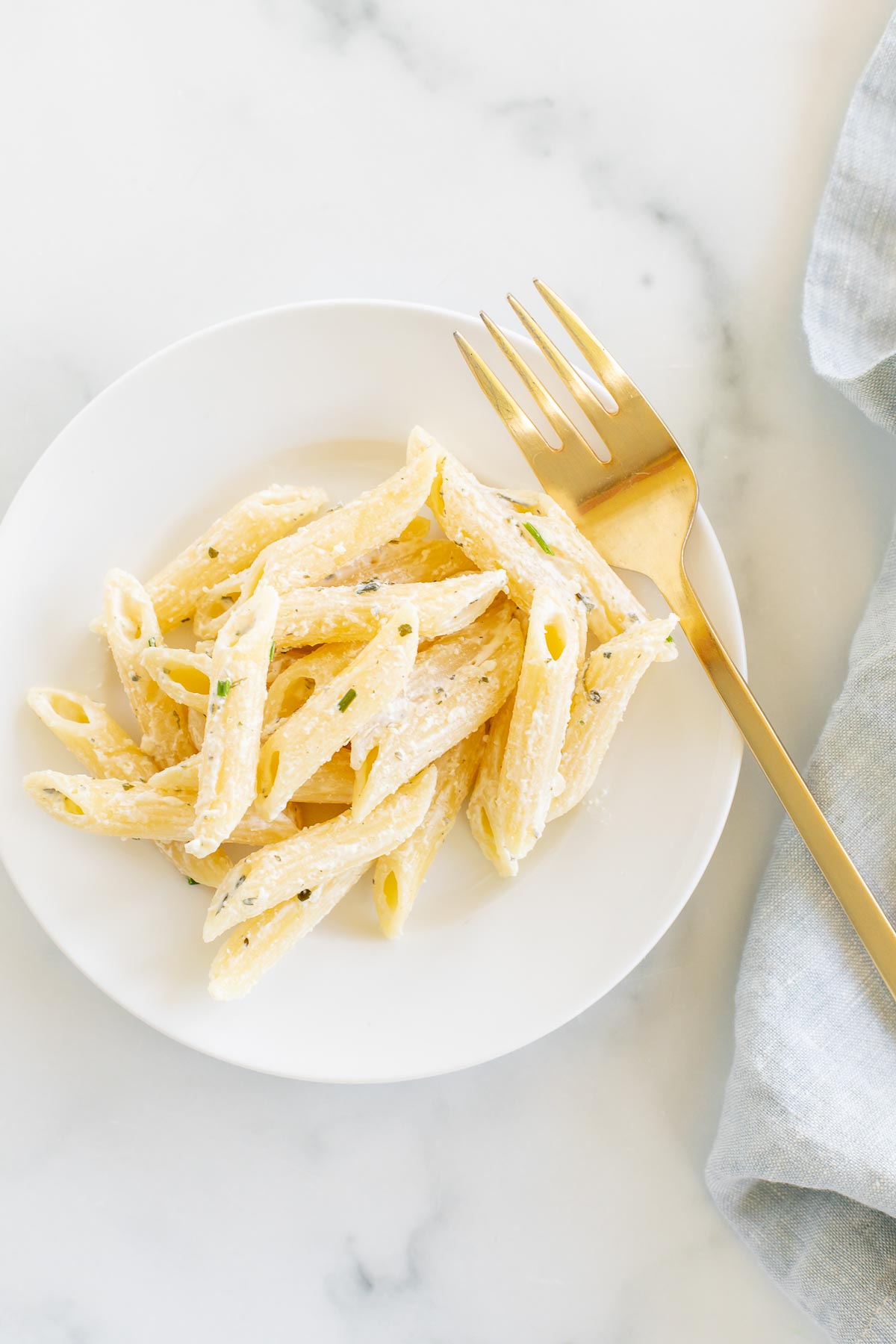 A white serving bowl full of Boursin pasta topped with chives.