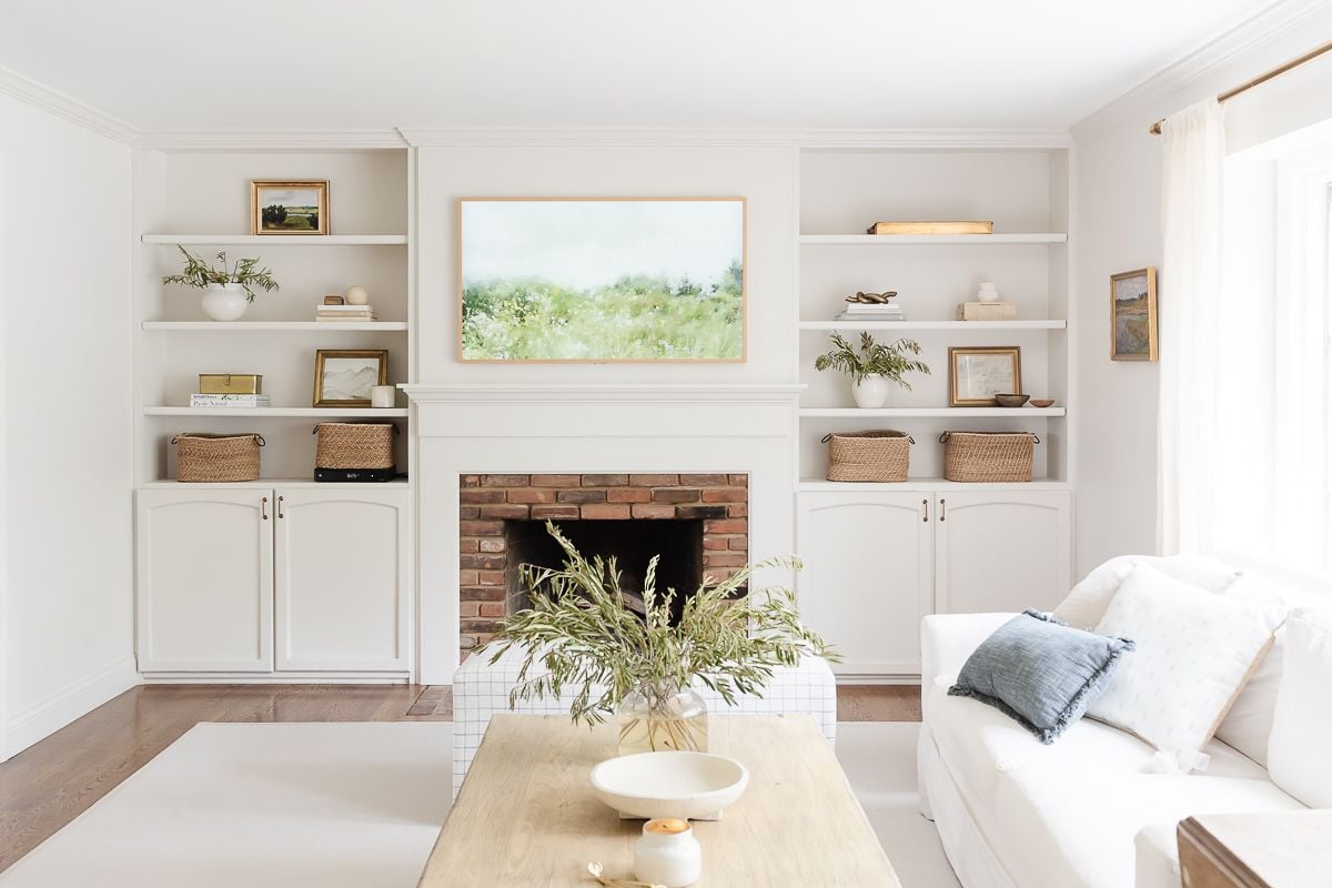 A white living room with built in bookshelves around a brick fireplace.