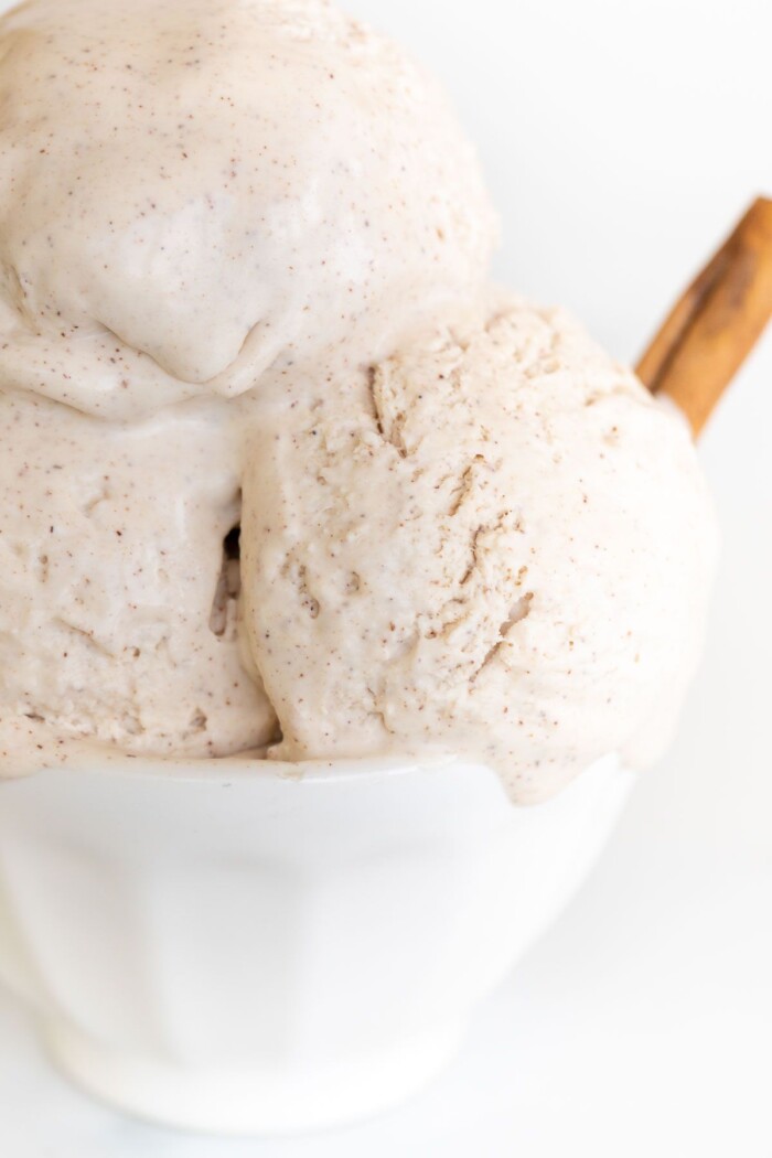 A white bowl full of homemade cinnamon ice cream with a cinnamon stick as garnish on the side