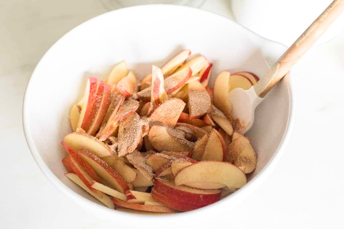 Baked apple slices in a white bowl with a wooden spoon.