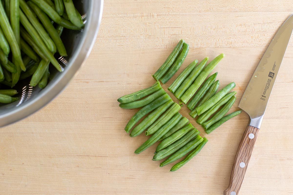 A wooden surface with sliced green beans and a knife to the right.