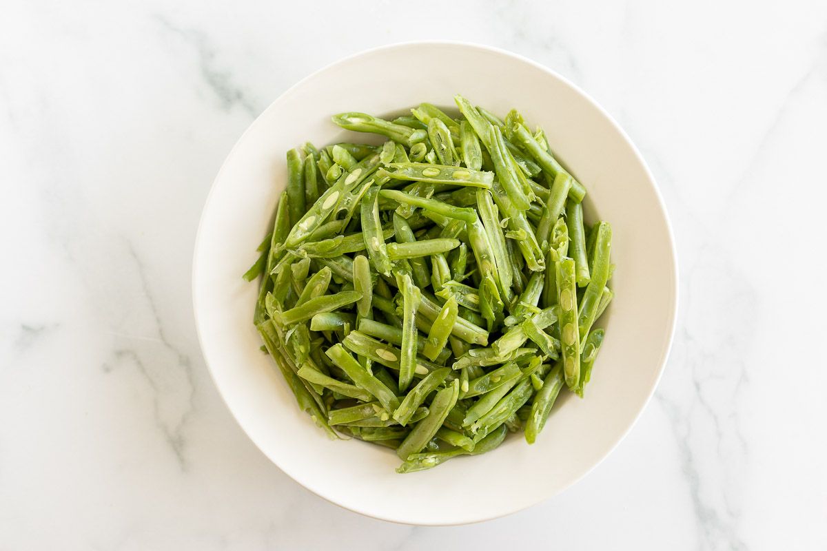 A white bowl on a marble surface, filled with French green beans.