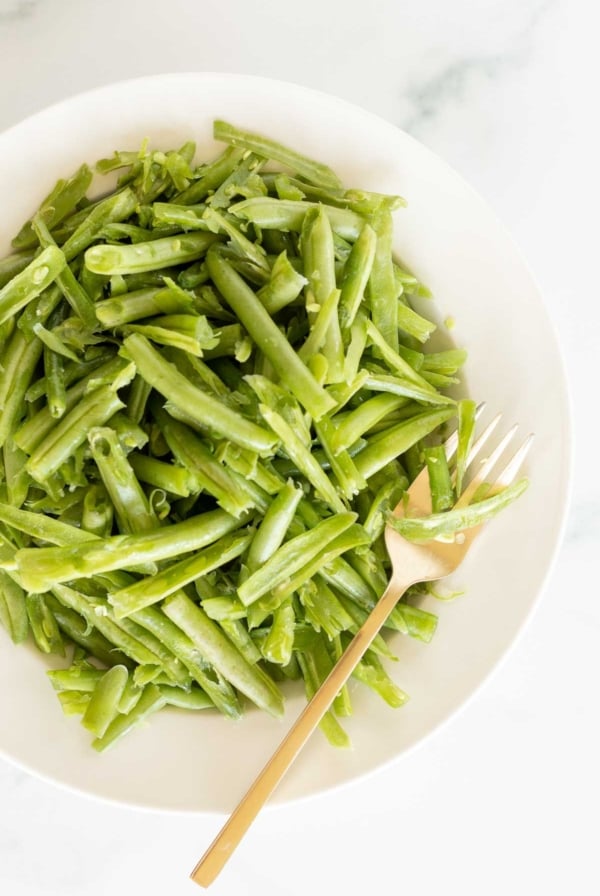 A white bowl on a marble surface, filled with French green beans.