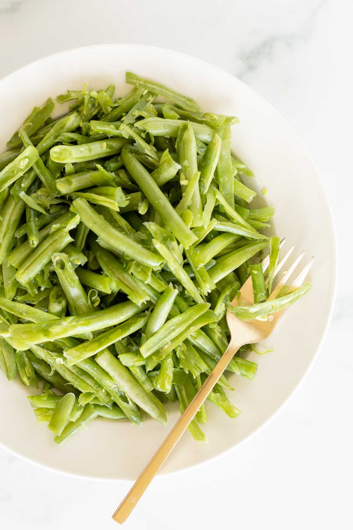 A white bowl on a marble surface, filled with French green beans.